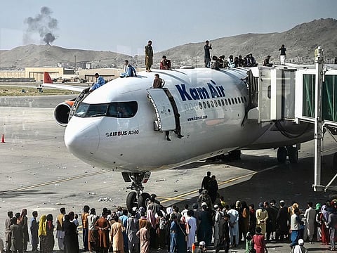 Afghan people climb atop a plane as they wait at the Kabul airport in Kabul on August 16, 2021, after a stunningly swift end to Afghanistan's 20-year war, as thousands of people mobbed the city's airport trying to flee.