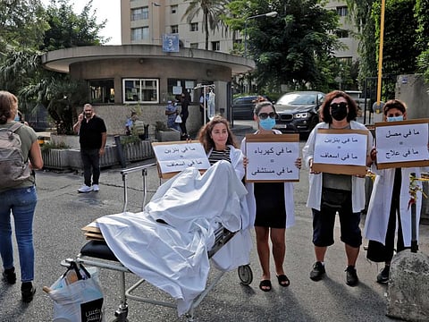 A pharmacist sits on a stretcher holding a sign reading in Arabic "no gasoline = no ambulance" while others stands by holding signs reading reading (left to right) "no electricity = no hospital" and "no vaccine = no treatment" as they stage a demonstration in the Achrafieh district of Lebanon's capital Beirut.