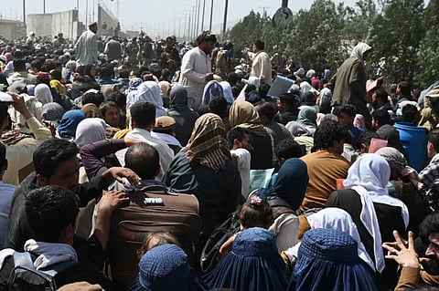 Afghans gather on a roadside near the military part of the airport in Kabul on August 20, 2021, hoping to flee from the country after the Taliban's military takeover of Afghanistan.