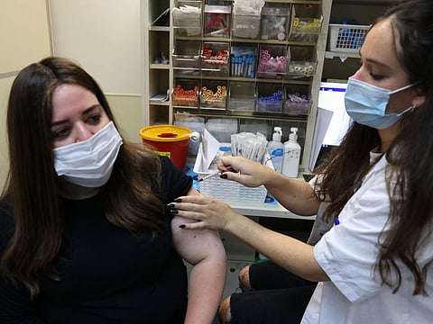 An Israeli health worker administers a third dose of the Pfizer-BioNtech COVID-19 vaccine to a woman, at the Maccabi Health Service in Jerusalem on August 20, 2021.