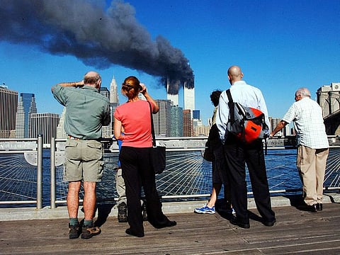 In this file photo pedestrians standing on the Brooklyn waterfront look across the East River towards the burning twin towers of the World Trade Center in lower Manhattan, New York on September 11, 2001.