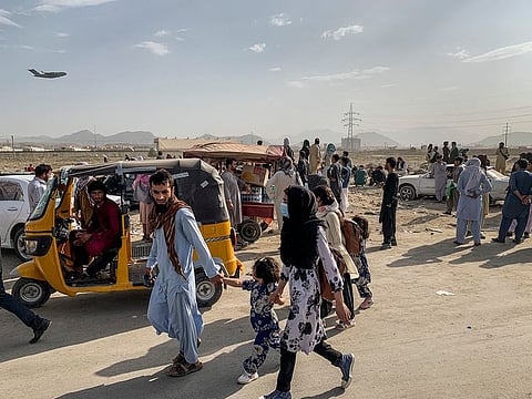 People wait outside Hamid Karzai International Airport as a military transport plane takes off behind them in Kabul, Afghanistan, Aug. 21, 2021.