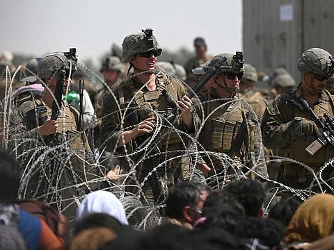 US soldiers stand guard behind barbed wire as Afghans sit on a roadside near the military part of the airport in Kabul on August 20, 2021