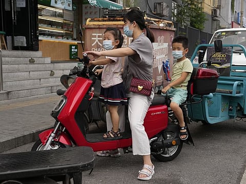 A woman transport two children on an electric bike in Beijing. China’s exam-oriented system previously required students to take exams from first grade onwards, culminating in the feared university entrance exam at age 18 known as the gaokao, where a single score can determine a child’s life trajectory.