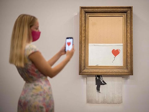 A visitor poses by an artwork titled ‘Love is the Bin’ by British street artist Banksy during a photocall at Sotheby’s auction house in central London.