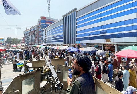 A Taliban fighter stand guard as people walk past a money exchange market in Kabul on September 4, 2021.