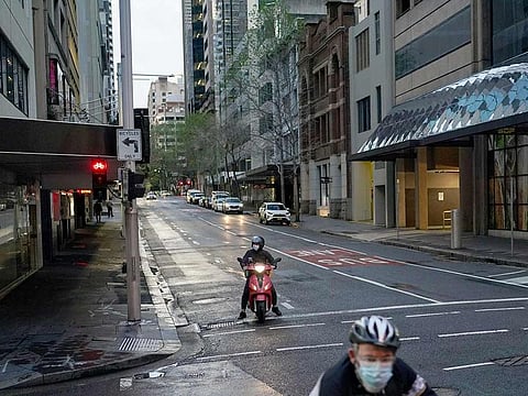A delivery courier on motorbike and a cyclist, both wear protective face masks, navigates the city centre in Sydney, on September 14, 2021.