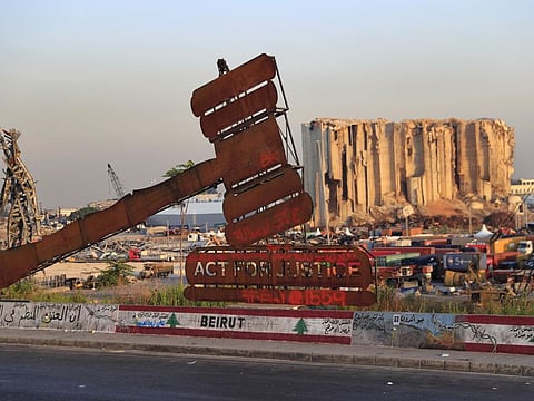 A justice symbol monument in front of towering grain silos in Beirut port that were gutted in the massive explosion last August.