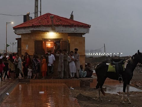 People shelter next to a building during a rainfall in Karachi on September 30, 2021, after Pakistan's authorities issued a warning that the rain-bearing system could be transformed into a cyclonic storm Gulab.