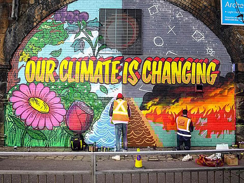 Street artists paint a mural on a wall opposite the COP26 climate summit venue in Glasgow on October 13, 2021