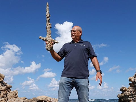 Jacob Sharvit of the Israel Antiquities Authority displays an ancient one-metre-long sword that experts say dates back to the Crusader-era and is believed to have belonged to a Crusader, displayed at the beach in the Israeli seaport of Caesarea, on October 19, 2021 some days after being discovered by a local diver.