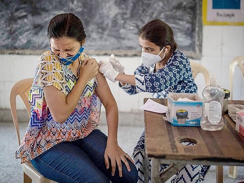 A woman reacts as a health worker inoculates her during a vaccination drive against coronavirus inside a school in New Delhi.