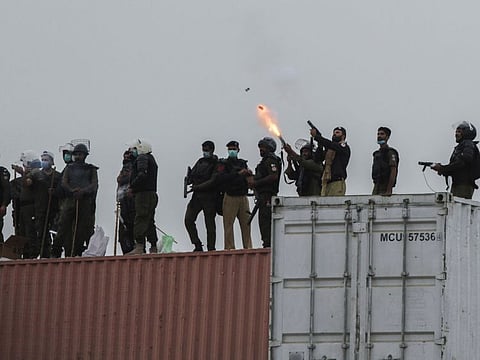 Police officers launch tear gas while stand on shipping containers used to block the road during a protest rally by the banned Islamist political party Tehrik-e-Labaik Pakistan in Lahore.