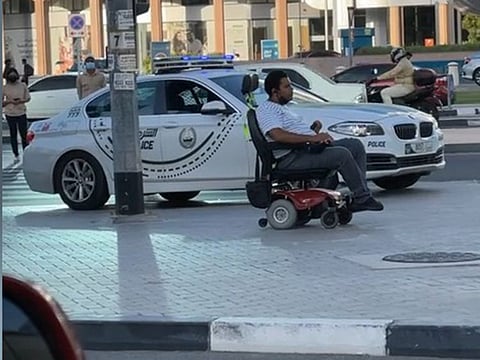 A Dubai Police patrol car escorts a person of determination while crossing the road.