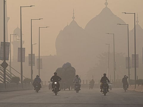 Commuters ride along a road amid smoggy conditions in Lahore on November 16, 2021.
