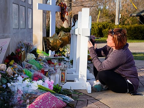 A woman writes a message to a deceased friend on a memorial cross after a car plowed through a holiday parade in Waukesha, Wisconsin, U.S., November 23, 2021.