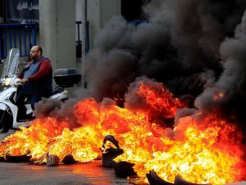 A man rides his scooter past burning tires at one of main roads during a protest against the increase in prices of consumer goods and the crash of the local currency, in Beirut on Monday.