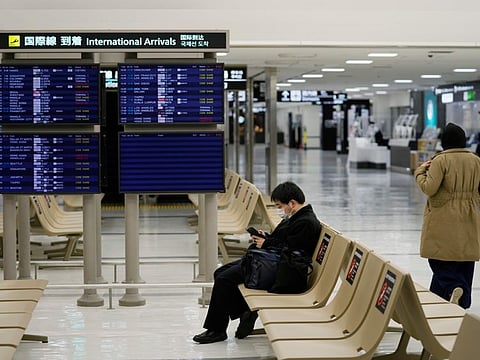 A passenger rests near arrival information screens for international flights at the Narita International Airport in Narita, east of Tokyo, Thursday, Dec. 2, 2021.