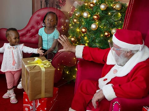 A child reaches out to Santa who wears a face shield as they are divided between a sheet of plastic, to protect against COVID-19 infection, at a Johannesburg mall.