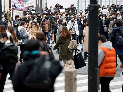People walk along a pedestrian crossing at Shibuya district on December 17, 2021, in Tokyo.