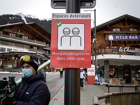 A picture taken on December 21, 2020, shows a ski tourist wearing a protective face mask amid the COVID-19 pandemic, walking past a sign reading in French: "Outdoor spaces, mask mandatory in this area", in the Swiss Alpine resort of Verbier, well known by british ski holiday makers.