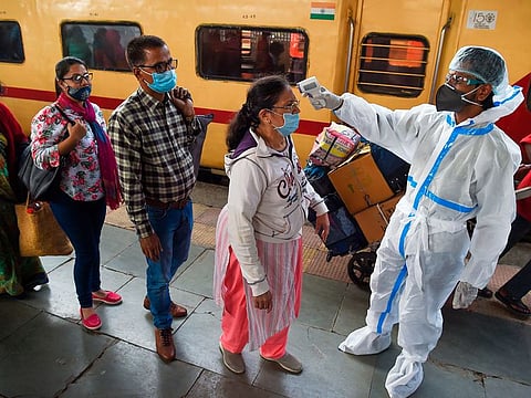 A health worker wearing protective gear checks the body temperature of passengers upon their arrival at the railway platform in Mumbai.