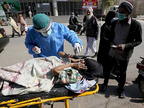 A health care worker takes a nasal swab sample from a woman at a COVID-19 testing facility at a hospital in Islamabad, Pakistan.