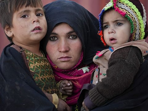 An Afghan woman holds her children as she waits for a consultation outside a makeshift clinic organised by World Vision in an IDP settlement near Herat, Afghanistan o December 16, 2021. Thousands of Afghans displaced by war and drought live in dire conditions in the IDP settlement of mud-brick huts near Herat city.