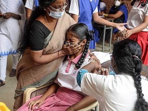 A teacher holds a student as a health worker inoculates her with a COVID-19 coronavirus vaccine during a vaccination drive for people in the 15-18 age group, at a girls high school in Hyderabad on January 6, 2022.