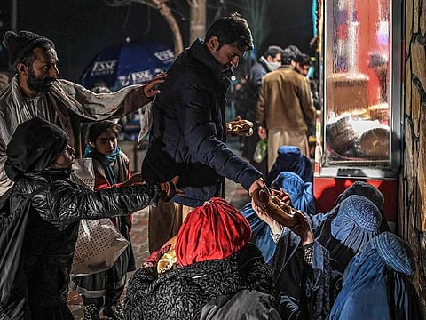 A man distributes food to burqa clad Afghan women sitting in front of a bakery in Kabul