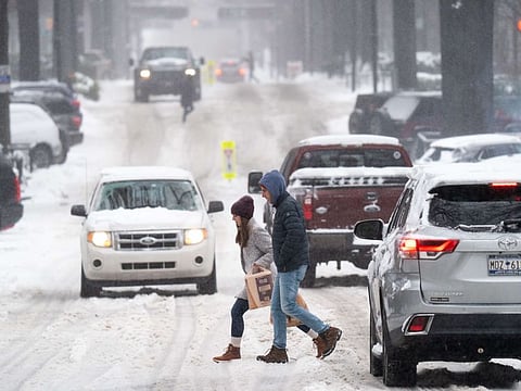 Pedestrians cross a street as motorists drive through the snow on January 16, 2022 in Greenville, South Carolina. The winter storm brought snow, sleet and freezing rain to parts of the Carolinas and Georgia where it left nearly 200,000 without power.