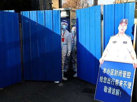 Workers wearing protective suits stand at an entrance to a residential compound under lockdown after a case of the Omicron variant was detected, in Beijing's Haidian district, on January 18, 2022.