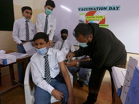 A student receives a dose of Pfizer coronavirus vaccine from a health worker while others wait their turn at a school in Karachi, Pakistan, Monday, Jan. 24, 2022.