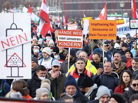 People demonstrate with placards reading "Hands off our children" and at (right) "Compulsory vaccination for recovered people is Nazi-terror 2021" against the Austrian government's measures taken in order to limit the spread of the COVID-19 during a protest in Vienna on January 8, 2022.