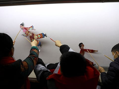 Shadow play troupe members showcase puppets made for a Winter Olympics-themed show behind a screen at the Longzaitian, or Dragon in the Sky, shadow puppet theatre in Beijing.