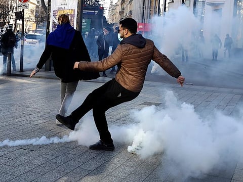 A demonstrator kicks a tear gas grenade during a protest on the Champs-Elysees avenue, on February 12, 2022 in Paris.