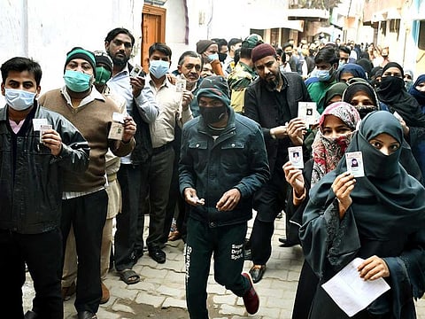 Voters show their voter ID cards while standing in queues to cast votes during the second phase of Uttar Pradesh Assembly elections, at a polling booth, in Moradabad on Monday, Feb 14, 2022.