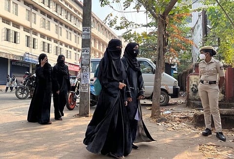 Hijab wearing schoolgirls arrive to attend their classes as a policewoman stands guard outside a government girls school after the recent hijab ban, in Udupi town in the southern state of Karnataka, India, February 16, 2022.