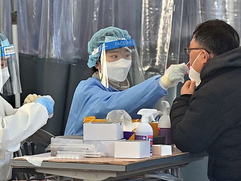 A medical worker (C) takes a nasal swab sample from a man at a Covid-19 coronavirus testing centre in Seoul on February 18, 2022, after South Korea's daily Covid-19 caseload crossed 100,000 for the first time.