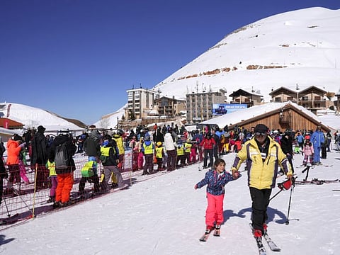 A man holds a child's hand as he walks through snow with ski equipment at a ski resort in Kfardebian, Lebanon, February 13, 2022.