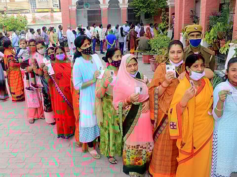 Women voters show their IDs while waiting in a queue to cast their votes for the seventh and final phase of the Uttar Pradesh Assembly Elections, at a polling station, in Varanasi on Monday, Mar 7, 2022.