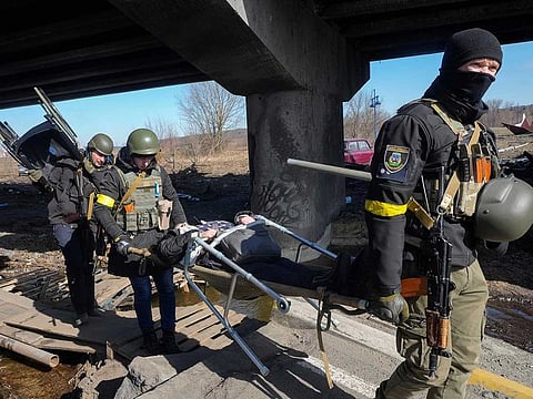 Ukrainians soldiers pass an improvised path under a destroyed bridge as they evacuate an elderly resident in Irpin, some 25 km northwest of Kyiv, Friday, March 11, 2022.