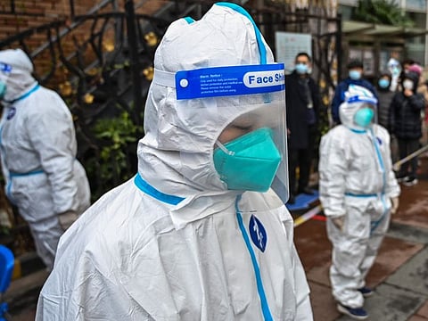Workers wearing protective gear look on as people wait to be tested for the Covid-19 coronavirus at a residential compound in Shanghai on March 18, 2022.
