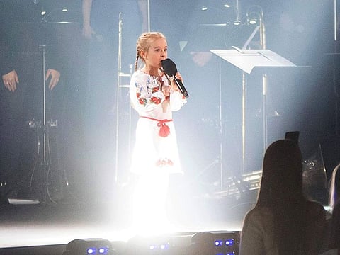 Seven-year-old Amellia Anisovych, a refugee from Ukraine, center, sings the Ukraine national anthem at the start of a fund-raising concert in Lodz, Poland