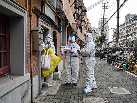 Health workers wearing protective gear as a measure against the Covid-19 coronavirus work along a street in Jing'an district in Shanghai on March 26, 2022.