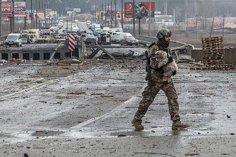 A Ukrainian service member carries a dog next to a destroyed bridge over the Irpin river, as Russia's attack on Ukraine continues, in the town of Irpin, Kyiv region, on March 30, 2022.