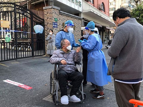 Workers in protective gear help a man in a wheelchair during the mass testing for residents in a lockdown area in the Jingan district of western Shanghai Monday, April 4, 2022.