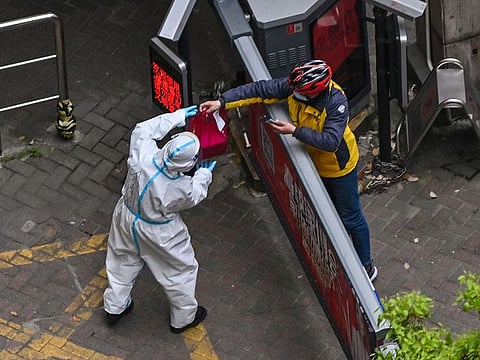 A worker wearing protective gear (L) receives an item from a delivery worker at the entrance of a compound during the second stage of a pandemic lockdown in Jing' an district in Shanghai on April 5, 2022.