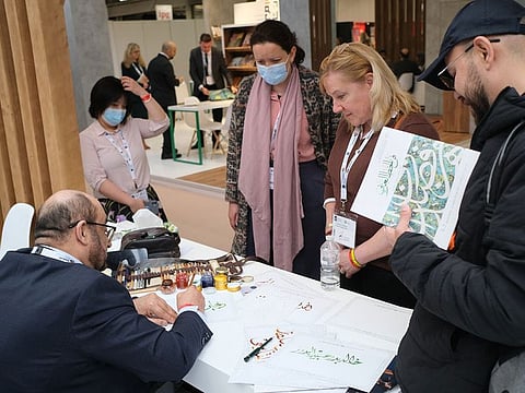 Emirati calligrapher Khalid Al Jallaf at work at LBF 2022 as visitors look on.