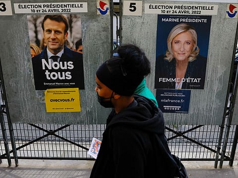 People walk past official campaign posters of French presidential election candidates Marine le Pen, leader of French far-right National Rally (Rassemblement National) party, and French President Emmanuel Macron, candidate for his re-election, displayed on bulletin boards in Paris, France, April 4, 2022.